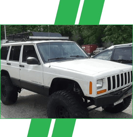 A white jeep cherokee with large tires parked in a parking lot.